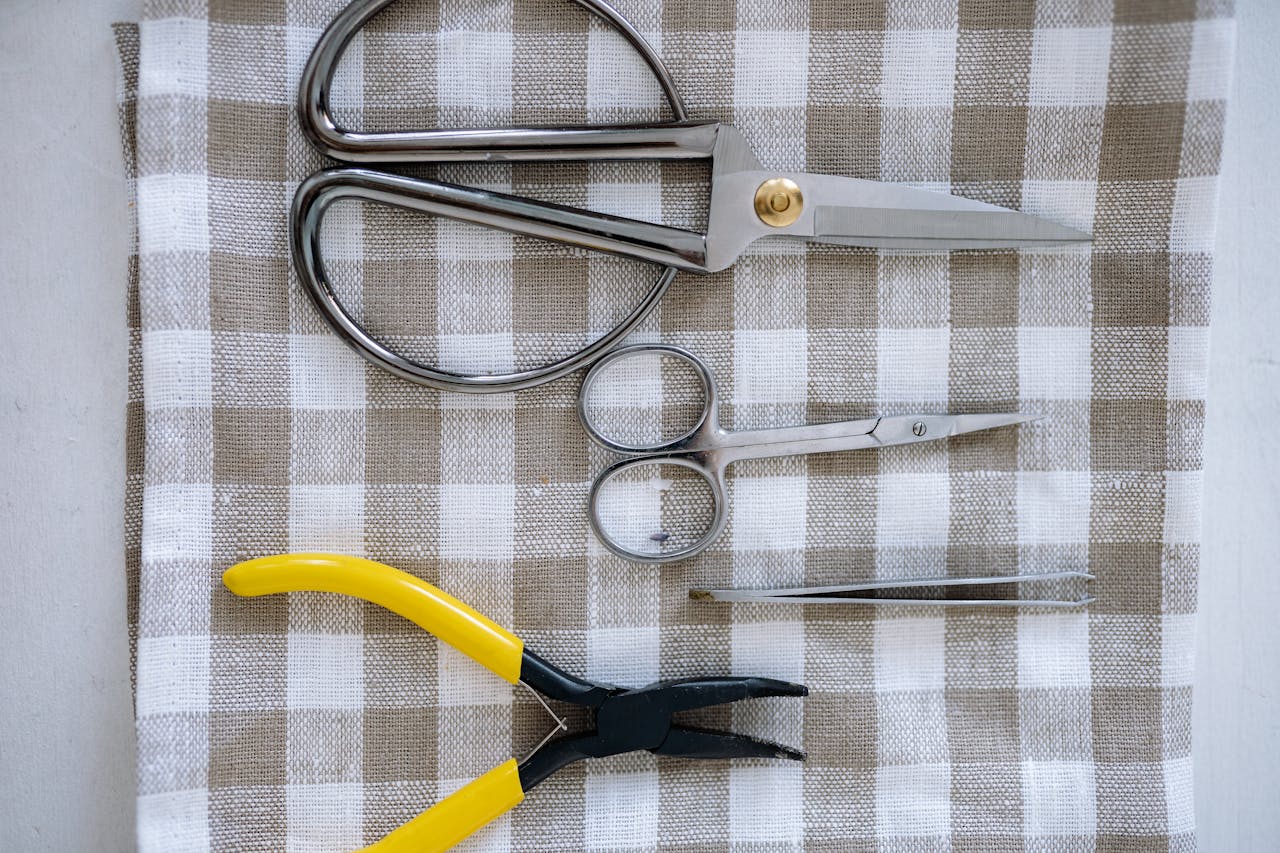 Flat lay of metal scissors and pliers on a checkered cloth for crafting or sewing.