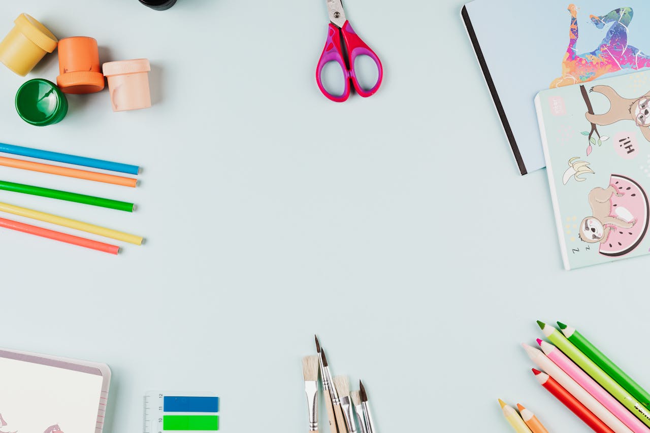 A creative flat lay of colorful art supplies arranged on a light blue background with copy space.
