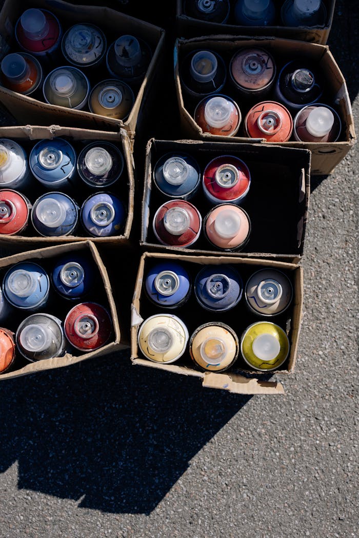 Top view of various spray paint cans organized in cardboard boxes on pavement.